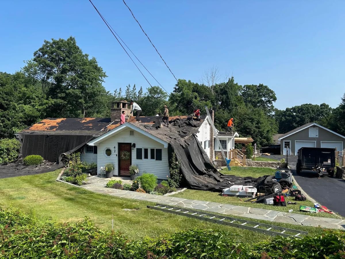 Tear-off in progress with tarps and a dumpster staged on the driveway