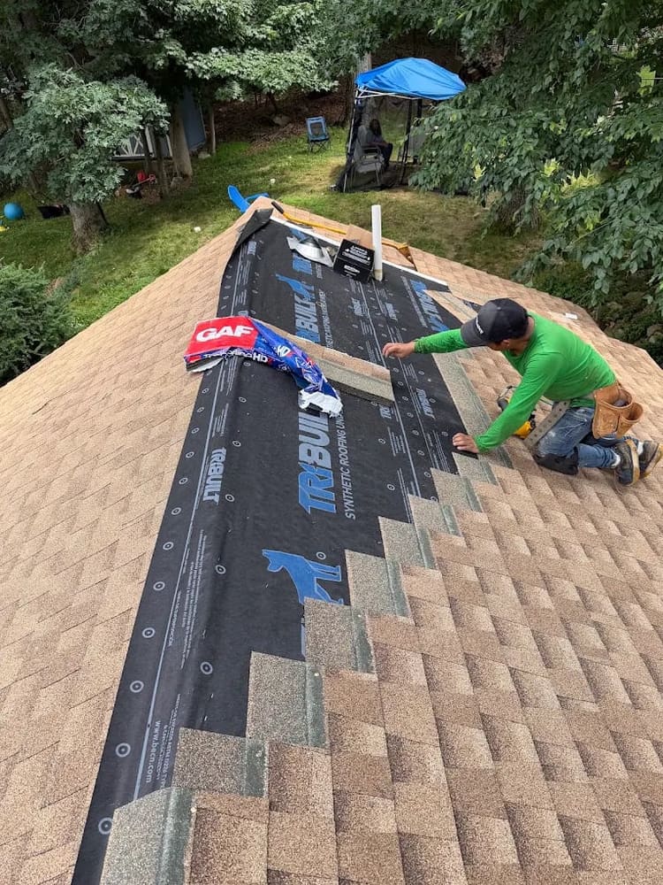 Roofer nailing architectural shingles over synthetic underlayment