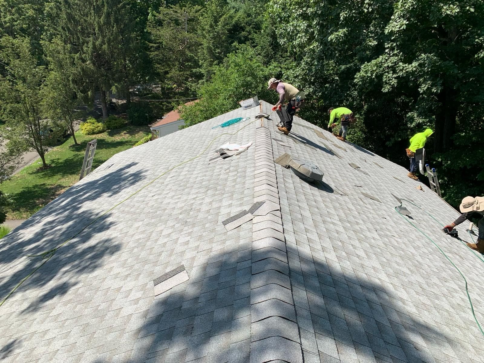 Asset crew installing architectural shingles on a steep roof under mature trees in North New Jersey