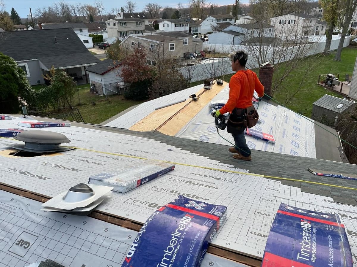 Roofer rolling out synthetic underlayment over new decking before shingles go on